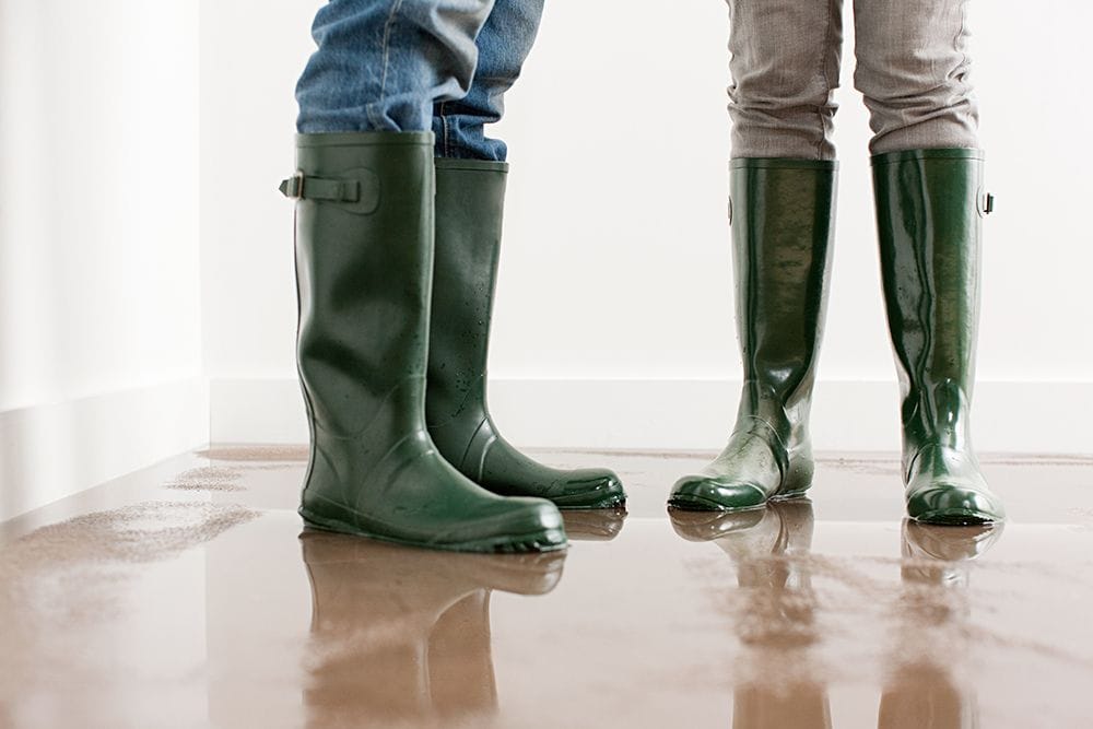 People stand in a puddle with boots. What to Do When Your Furnace Is Leaking Water.