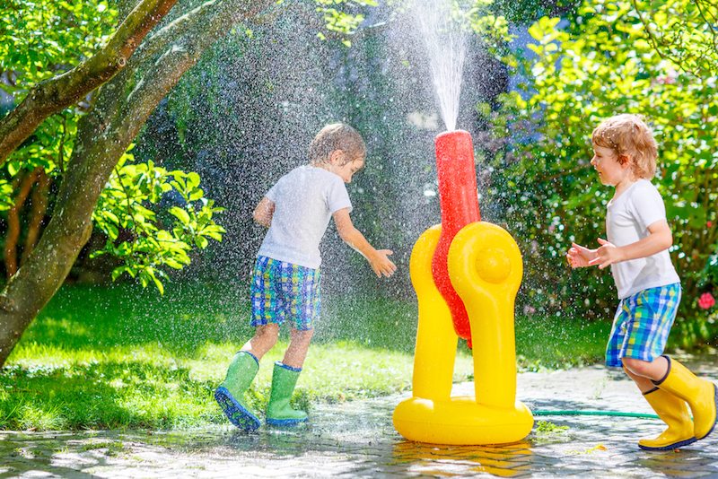 Two boys running through a sprinkler and are managing humidity in Athens