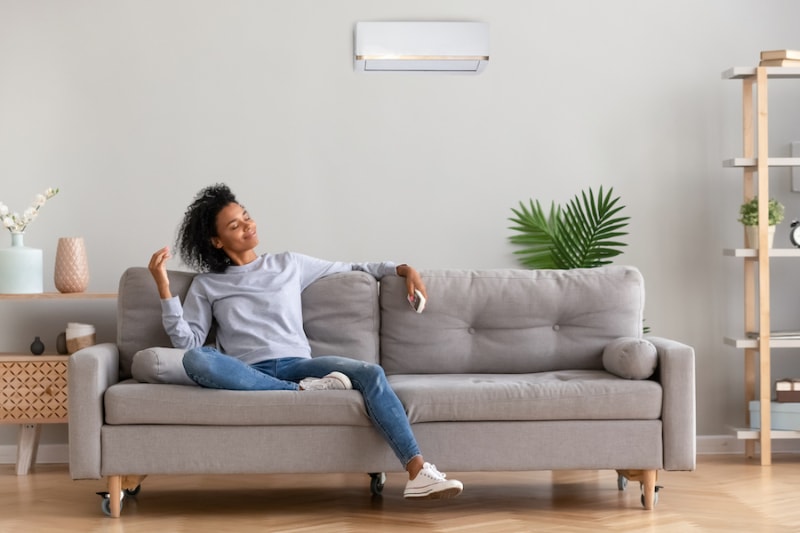 Woman in living room sitting on couch, enjoying the benefits of ductless mini splits. Airclaws blog image.