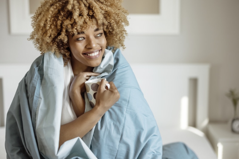 Woman enjoying a cup of tea while wrapped in duvet after having her furnace maintenance completed. Airclaws blog image.