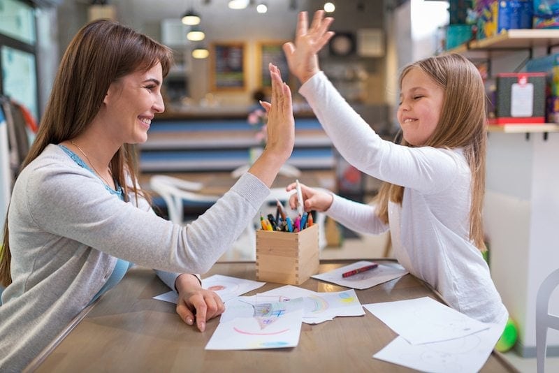 Mother and daughter high-fiving across a kitchen table. They know the importance of air conditioner maintenance in Athens